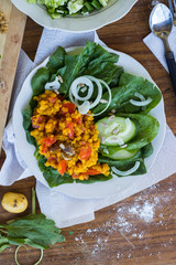 Red Indian cooked lentil beans with tomatoes, turmeric powder and spices. Served with fresh green vegetables: cucumbers, onion rings, spinach leaves Raw vegan vegetarian food. Healthy lunch, dinner