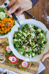 Woman hands holds and mix green vegetables fresh summer salad with cabbage, spinach leaves, onion and walnuts. Raw vegan vegetarian healthy food