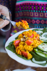 Woman hands holds red Indian cooked lentil beans with tomatoes, turmeric powder and spices. Served with fresh green vegetables: cucumbers, onion rings, spinach leaves Raw vegan vegetarian food. 