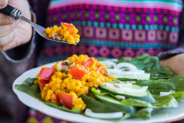 Woman hands holds red Indian cooked lentil beans with tomatoes, turmeric powder and spices. Served with fresh green vegetables: cucumbers, onion rings, spinach leaves Raw vegan vegetarian food. 