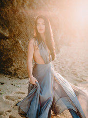 Fototapeta na wymiar Portrait of brunette bride in blue wedding dress at beach with sunset or sunrise colors