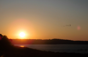 Sunset on the horizon in orange color and flock of birds. Lake of the Hydroelectric Power Plant of Emboracação in Minas Gerais, Brazil.