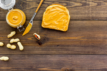 Spread nut butter on sandwich. Toast, knife and glass jar with nut paste, nuts on dark wooden background copy space