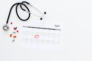 Planning medical examination concept. Regular medical examinations. Calendar with date circled, pills and stethoscope on white background top view copy space