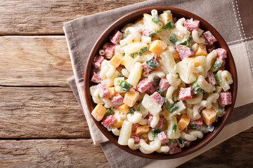 Hawaiian food: salad with pasta, ham, pineapple, onion, cheddar cheese with mayonnaise close-up in a bowl. horizontal top view