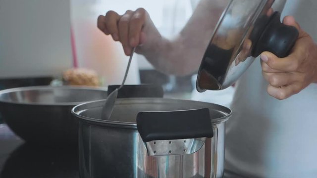 Hand with spoon stirring boiling soup, close-up.