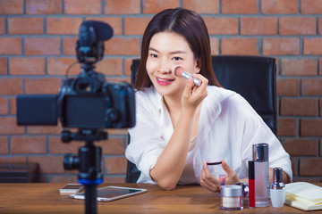 Young happy asian woman online cosmetic seller vlogging to her fan page showing how to put make up on