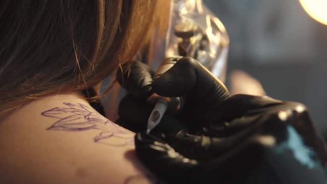 a girl tattoo artist is drawing a picture on the customer's body tattoo machine. tattoo master works in home studio