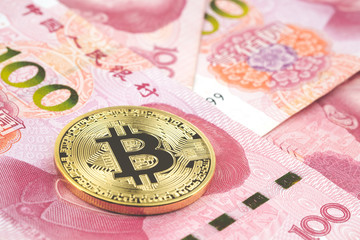 Golden bitcoin on pile of one hundred Chinese yuan banknotes background.