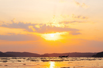Beautiful summer sunset over sea with sunbeam through clouds above mountain and fishing boat.
