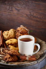 Conceptual festive composition with a cup of hot tea, cookies and spicies on a wooden barrel, selective focus, close-up