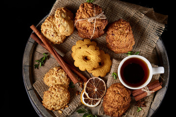 Top view festive composition with a cup of hot tea, cookies and spicies on a wooden barrel, selective focus, close-up