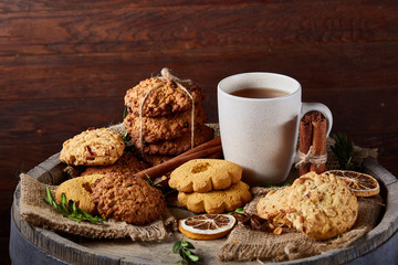 Conceptual festive composition with a cup of hot tea, cookies and spicies on a wooden barrel, selective focus, close-up