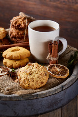 Conceptual festive composition with a cup of hot tea, cookies and spicies on a wooden barrel, selective focus, vertical