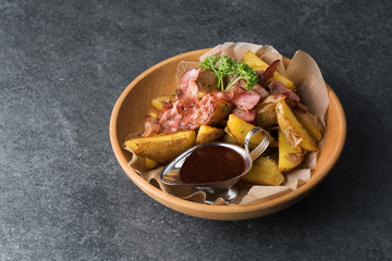 Fried potatoes with appetizing bacon and sauce are in a wooden plate