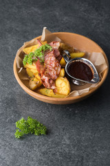 Fried potatoes with appetizing bacon and sauce are in a wooden plate