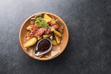 Fried potatoes with appetizing bacon and sauce are in a wooden plate