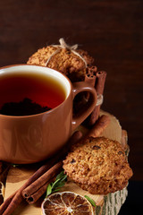 Christmas concept with a cup of hot tea, cookies and decorations on a log over wooden background, selective focus