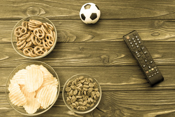 crackers, potato chips, TV remote control, soccer ball on a wooden background. sports fans