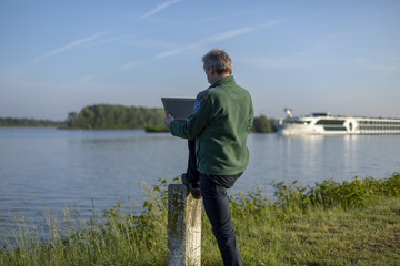 Mann steht am Rhein Iffezheim mit Laptop