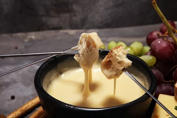Fototapete Gourmet Swiss fondue dinner on a winter evening with assorted cheeses on a board alongside a heated pot of cheese fondue © beats_