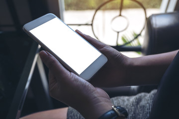 Mockup image of woman's hands holding white mobile phone with blank desktop screen sitting in cafe