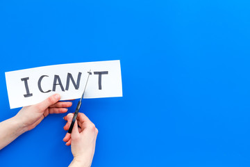 I can concept. Motivate youself, believe in yourself. Hand cut off the letter t of written word I can't by sciccors. Blue background top view copy space