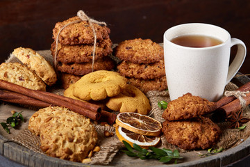 Conceptual festive composition with a cup of hot tea, cookies and spicies on a wooden barrel, selective focus, close-up