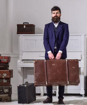 Baggage and travelling concept. Macho stylish on strict face stands and carries big vintage suitcase. Man, traveller with beard and mustache with baggage, luxury white interior background.