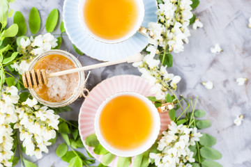 Vintage cups with tea next to a jar of honey and acacia on a gray table. Tea with natural sweetener honey. Top view, flat lay
