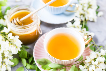 Vintage cups with tea next to a jar of honey and acacia on a gray table. Tea with natural sweetener honey