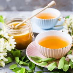 Vintage cups with tea next to a jar of honey and acacia on a gray table. Tea with natural sweetener honey