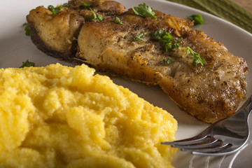 Fried fish woth polenta and herbs on plate with fork