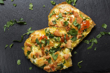 Delicious homemade fried egg in toast for breakfast with pieces of frankfurters, onion, cheese and herbs on slate