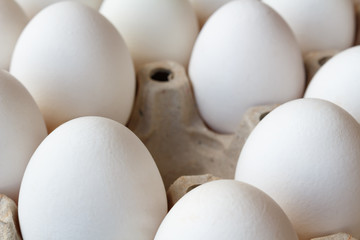 Empty slot among white chicken eggs in cardboard tray closeup