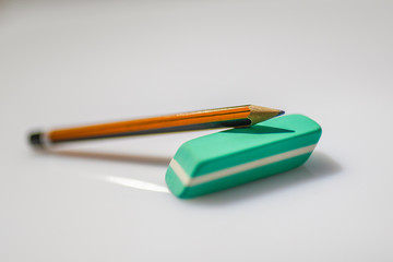 Pencil and eraser on white background. Close up of a orange and black wooden pen and an eraser green.