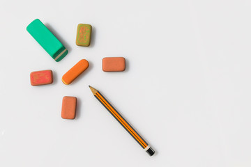 Wooden pencil and erasers like a flower on white background. Close up of a orange and black pen and six multicolors erasers 