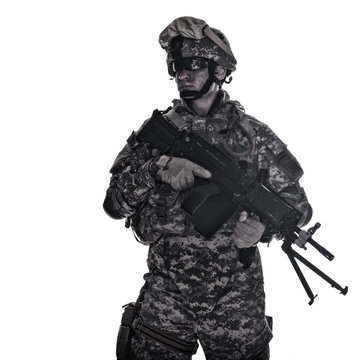 Low key portrait of United States Army Marine Corps fully equipped infantry soldier in sunglasses, helmet, heavy body armour standing with machine gun in hands desaturated isolated on white background