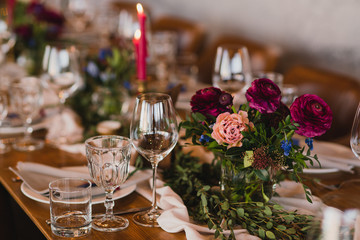 Coziness and style. Modern event design. Table setting at wedding reception. Floral compositions with beautiful ranunculus flowers and greenery, candles, laying and plates on decorated table.