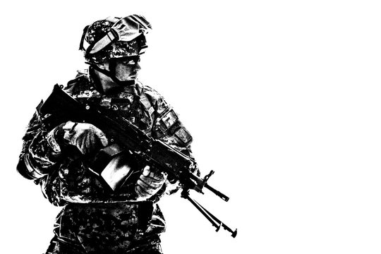 Low key side portrait of US Army Special Forces soldier in military camouflage uniform protected with helmet, body armour, holding machine gun desaturated, isolated on white background with copyspace