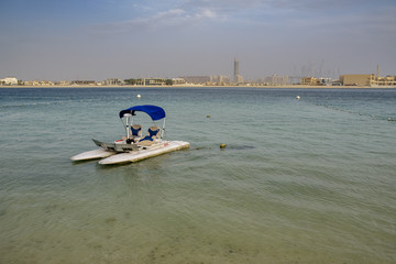 Naklejka premium small, single, pontoon boat, with a sun shade, floating near the shore, on a sun drenched beach, in Dubai