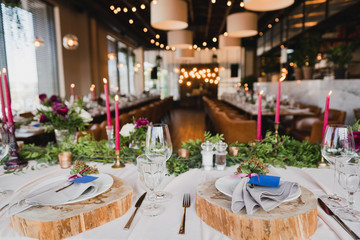 Coziness and style. Modern event design. Table setting at wedding reception. Floral compositions with beautiful ranunculus flowers and greenery, candles, laying and plates on decorated table.
