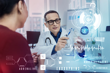 Detailed explanation. Clever professional doctor carefully explaining the problem while showing a heart miniature to his attentive patient