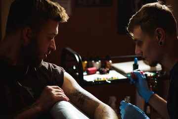 Professional tattoo artist makes a tattoo on a man's hand.