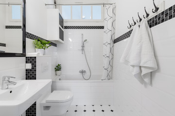 Towels and mirror in white and black bathroom with bathtub and toilet. Real photo