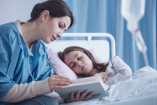 Mother reading book to sick sleepy daughter in the clinic