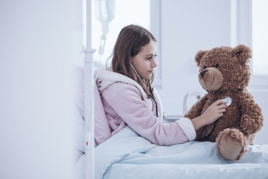 Sick girl with stethoscope examining teddy bear in the hospital bed
