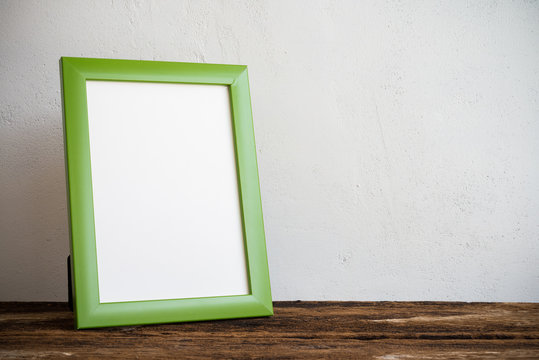 Green photo frame on old wooden table over white wall background