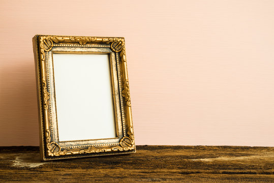 Golden vintage photo frame on old wooden table over pink wall background