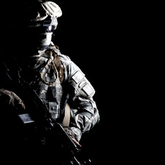 Armed army soldier in camouflage uniform, with hidden face, sneaking in dark during combat, counter...